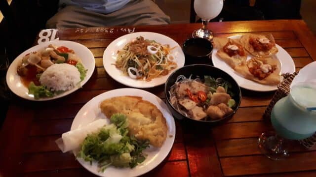 Five plates of assorted Asian cuisine on a wooden table, with two drinks in the background.
