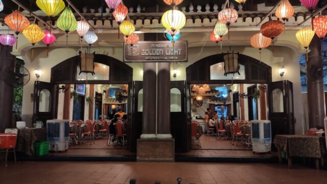 Restaurant in Hoi An with colorful lanterns hanging outside, open doors, and diners seated at tables inside.