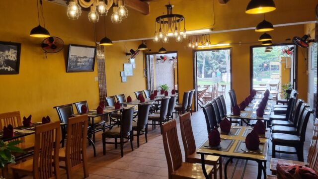 Cozy restaurant with yellow walls, wooden tables and chairs, napkins on tables, and hanging lights.