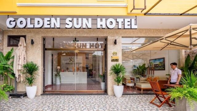 Golden Sun Hotel entrance with glass doors, potted plants, outdoor seating, and a guest standing nearby.
