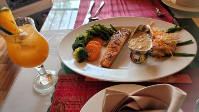 Grilled salmon with vegetables and sauce, served with a tropical drink on a Hoi An restaurant table.