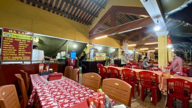 Hà Lan Restaurant is a casual Vietnamese spot with red chairs, patterned tablecloths, and a menu sign on the wall.