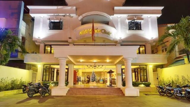 Brightly lit Hai Yen Hotel entrance at night, with columns, parked motorbikes, and a Christmas tree visible inside.