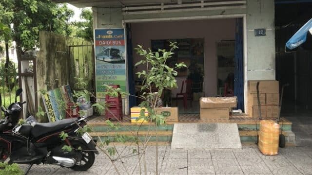 Travel agency storefront with motorbikes parked in front; signs advertise bus tours to Hoi An and other Vietnamese cities.