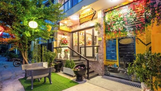 Hannah's House: A cozy, brightly lit café exterior with flowers, plants, and inviting outdoor seating at night.