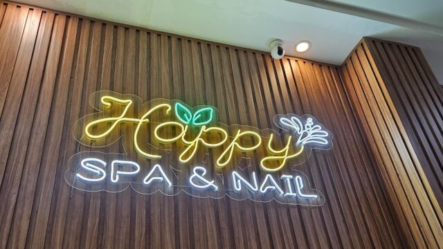 Neon sign reading Happy Spa & Nail on a wood-paneled wall, with leaf and branch decor, welcomes you to this inviting Nail Spa.