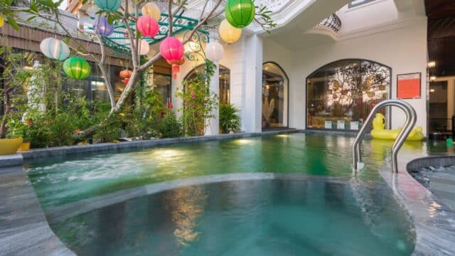 Small indoor pool with a metal ladder at Hoang Trinh Hotel, surrounded by plants and colorful lanterns hanging from a tree.