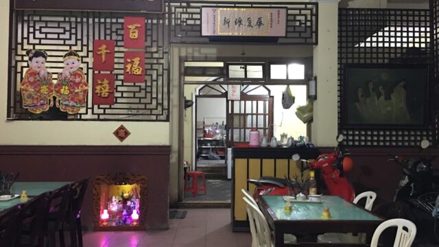 Interior of a Vietnamese restaurant in Hoi An with empty tables, vibrant decorations, and a view into the bustling kitchen area.