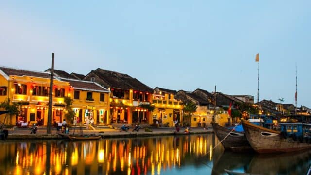 Colorful riverside buildings and boats reflected in the water at dusk on a Half Day Tour in Hoi An, Vietnam.