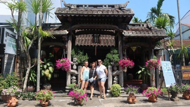 Three women pose in front of a traditional Hoi An building, surrounded by potted plants and flowers, ready for a Food Safari adventure.
