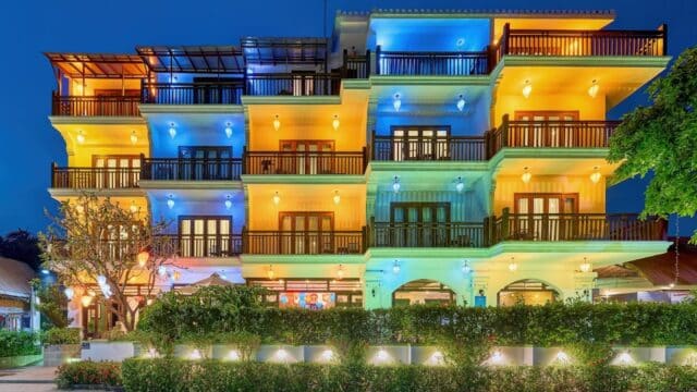 A brightly lit Odyssey Hotel in Hoi An with colorful lights on its balconies and facade at night.