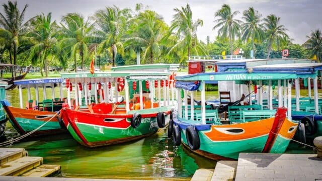 Colorful wooden boats docked by the riverside in Hoi An, with palm trees in the background—perfect for scenic River Boat Tours.