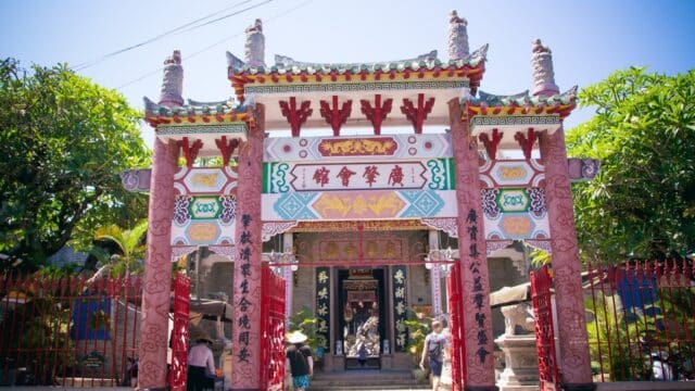 Colorful entrance gate to a Chinese temple in Hoi An, featuring decorative carvings and people walking inside.