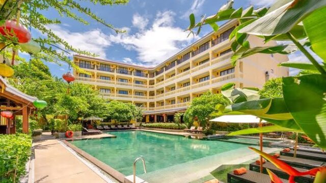 A sunny courtyard with a large pool, lush greenery, and a boutique hotel in Hoian featuring relaxing lounge chairs and a serene spa.