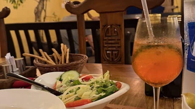 A table set with salad, pasta, breadsticks, and an orange drink in a cozy, warmly lit Italian Restaurant.