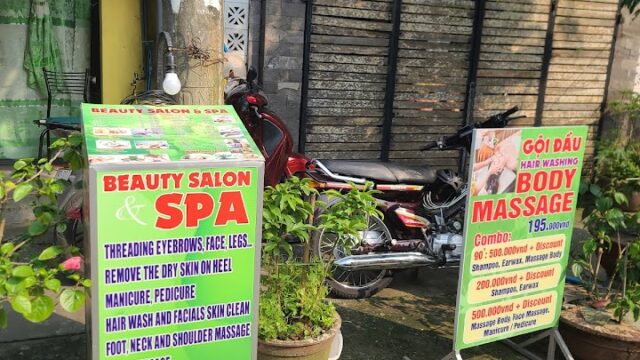Two signs outside a beauty salon and spa on a sidewalk, advertising various beauty and massage services.