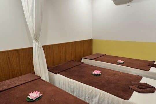 Three massage beds with brown sheets and lotus flowers await in the serene Ichi Spa room, promising total relaxation.