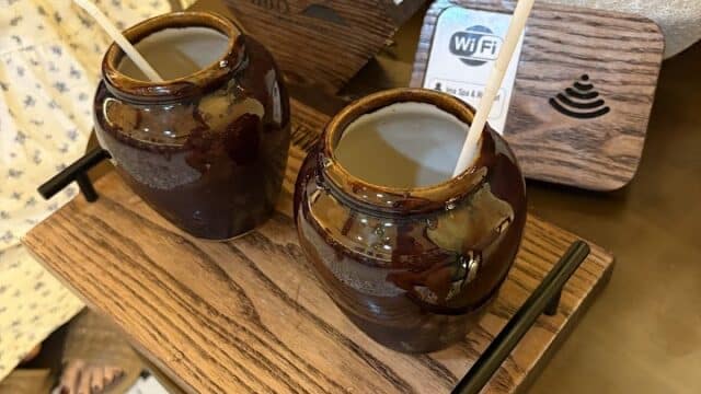 Two brown ceramic cups with straws on a wooden tray, perfect for a restful retreat at IMA Spa, sit beside napkins and a WiFi sign.