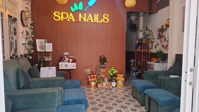 Cozy Kim Ngan Spa with teal chairs, floral decor, and a SPA. NAILS neon sign glows above a small offerings table on the wood wall.