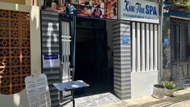 Entrance of a small spa named Kim Thu SPA with a manicure sample board outside on a sunny day.