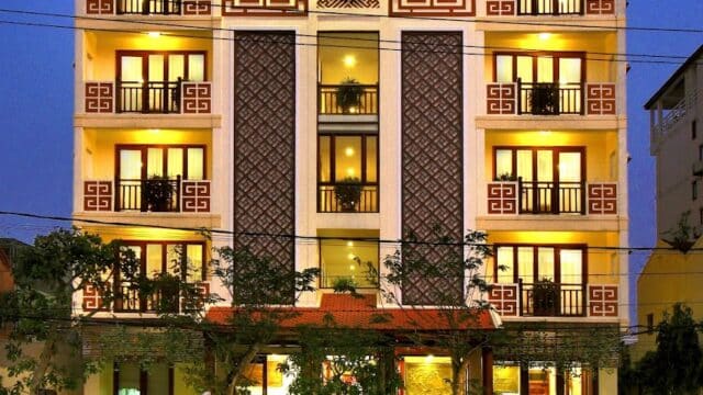 A warmly lit, multi-story hotel named Kiman Hotel with balconies and decorative facade at dusk.