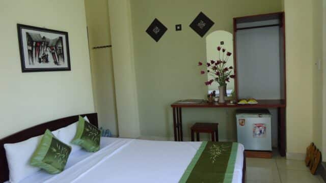 A tidy Kiman Old Town Hotel room with a bed, green accents, wall art, desk, mirror, fridge, and decorative flowers.