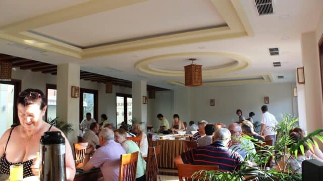 People dining in a brightly lit Hoi An restaurant with large windows and wooden furniture during daytime.
