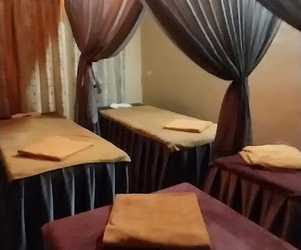 Four massage tables with folded towels in a softly lit room, separated by sheer curtains.