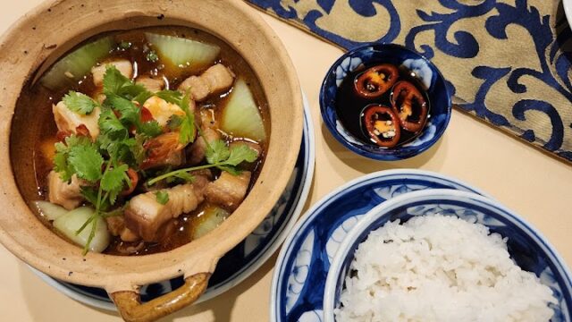Claypot dish with meat and vegetables, a bowl of white rice, and sliced red chilies at La Charm Restaurant on a patterned tablecloth.