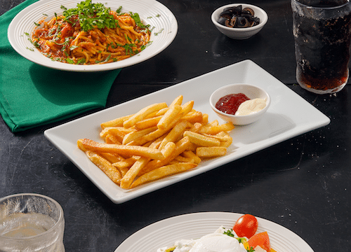 Pizza, pasta, fries with dips, salad, and drinks on a dark table set for a Hoi An-inspired meal.