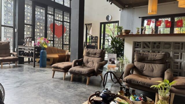 Cozy cafe with brown armchairs, tea set on a table, large windows, and Vietnamese flags behind the counter.
