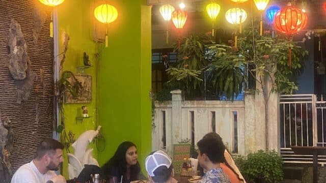 Five people dining at a brightly lit Hoi An restaurant with colorful lanterns and green walls, enjoying a meal together.