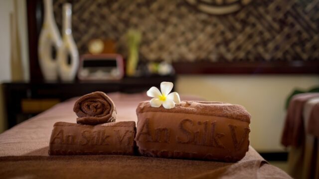 Brown towels with a white flower on top, set on a massage table in a spa with soft lighting.