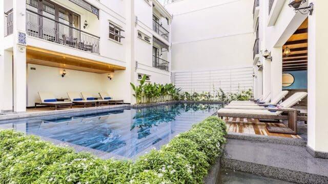 Outdoor pool with lounge chairs and greenery, next to the modern white Laluna Hotel and its relaxing hotel spa.