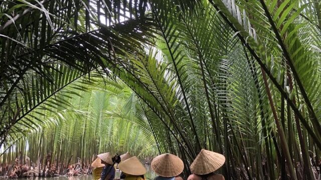 People in round boats wearing conical hats paddle through a lush Hoi An waterway lined with tall palms.