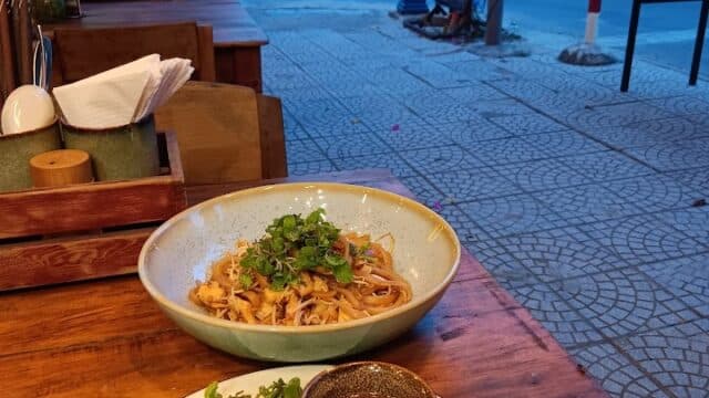 A wooden table with noodles, seaweed rolls, and dipping sauce at Lantern Eatery, an outdoor dining spot by the street.