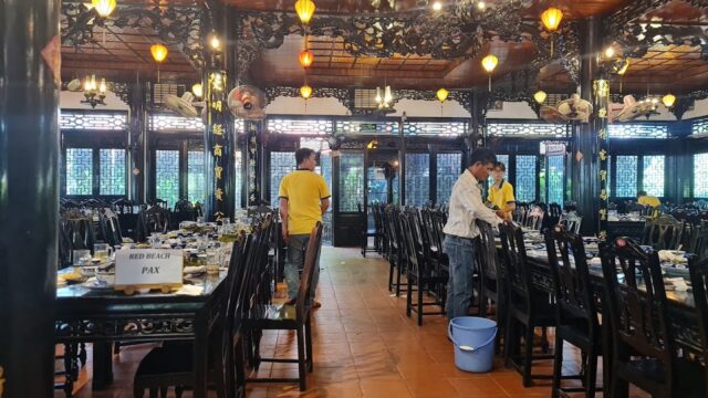Spacious Hoi An restaurant with wooden decor, set tables, and staff in yellow shirts preparing for guests.