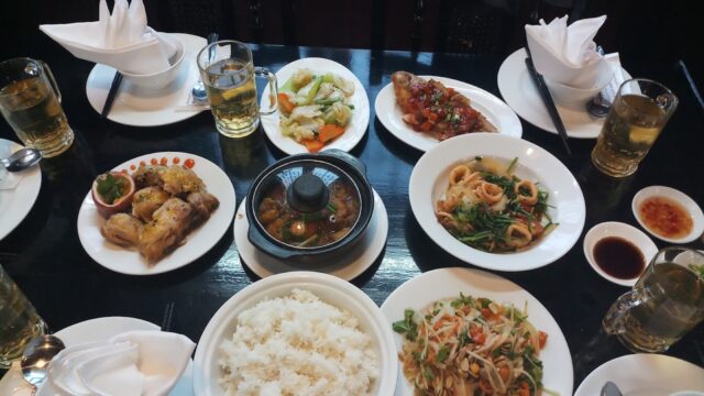 A table set with white rice, Asian dishes, and beer, captured in the signature style of Lê Bá Truyền.