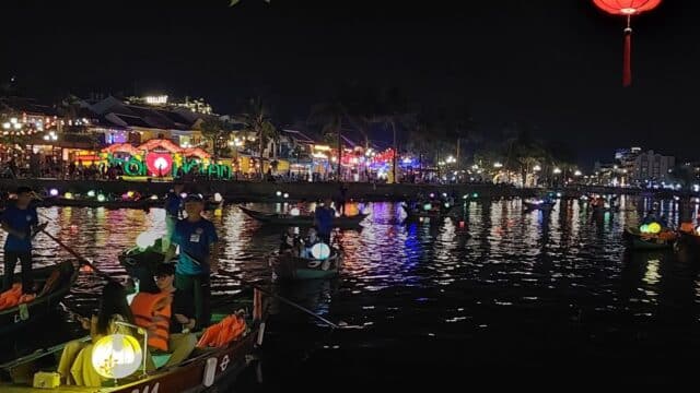 Colorful boats with lanterns float on a river at night—city lights shine above. Let’s Go Travel and experience this magical scene!