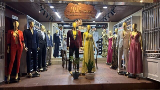 Mannequins in formal suits and dresses displayed outside a tailor shop at night, with a sign reading LINE Tailor.