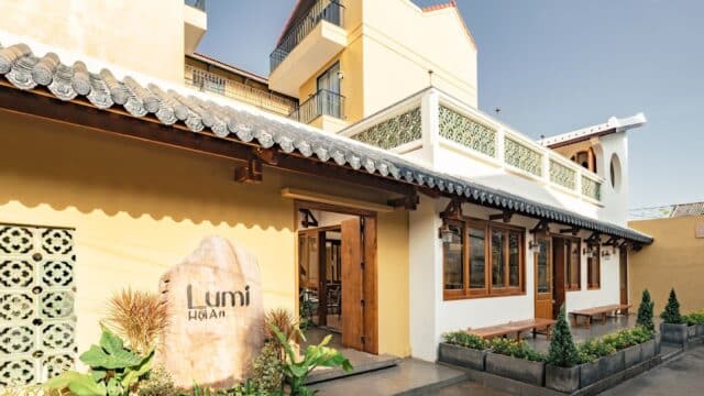 Yellow building with wooden doors and windows, a sign reading Lumi Hoi An, and potted plants outside.