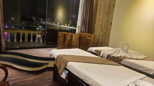 A serene spa room with two massage beds, wooden tubs, and towels folded into a heart shape.