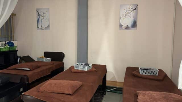 Three massage beds with brown towels and baskets in a calm, softly lit room with minimalist wall art.
