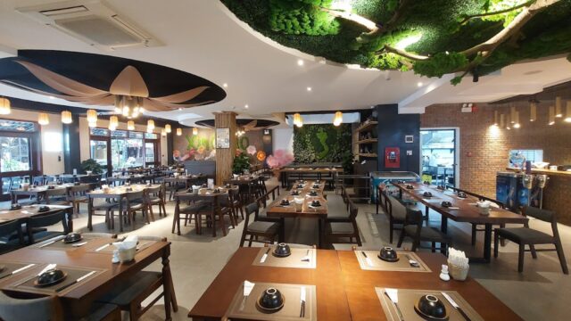 Spacious modern Madam Nga Restaurant with wooden tables, green plant decor on the ceiling, and warm ambient lighting.