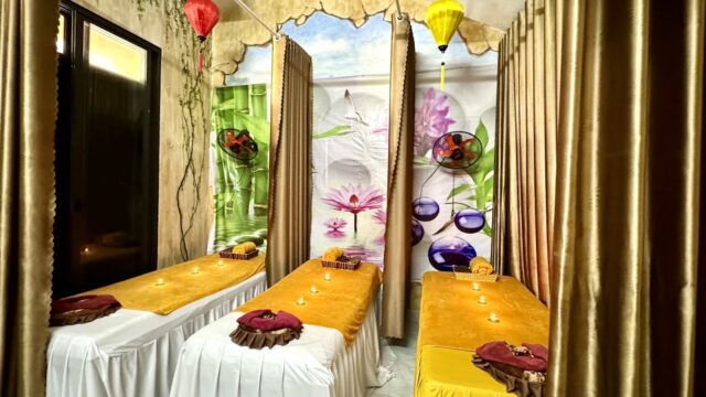 Two massage tables with golden covers, decorative lanterns, and floral wall art create a cozy retreat at Magnolia Spa.