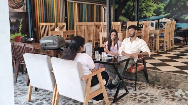 Three people sit at a table in a colorful, modern Hoi An café with a patterned tile floor and eclectic decor.