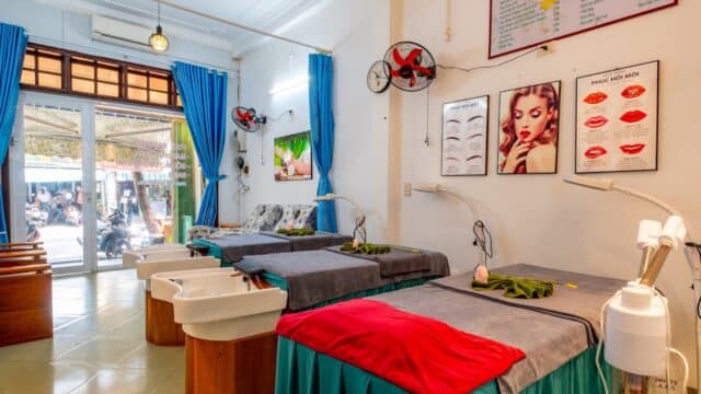 Three spa beds with towels and sinks in a bright, tidy beauty salon with posters and blue curtains.