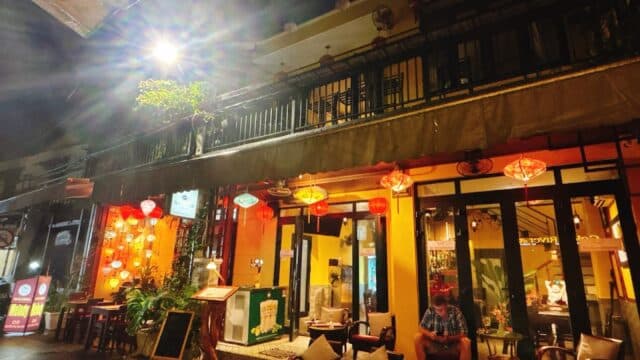 Cozy outdoor cafe at night with warm lighting, lanterns, and a person sitting under a covered seating area.