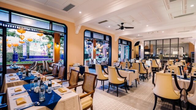 Elegant fine dining restaurant interior with neatly set tables, wooden chairs, and large windows overlooking lantern-lit melodies outside.