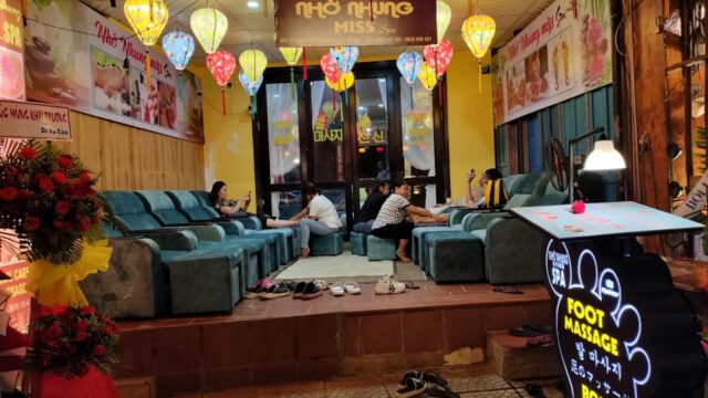 Several people relax in a brightly lit salon with colorful lanterns and a sign advertising foot massages.